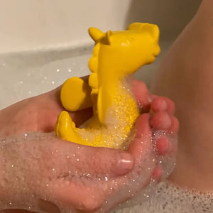 Lifestyle pic of yellow rubber seahorse bath toy cupped in a person's hands.