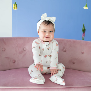 Lifestyle pic of baby with a cloud bow in her hair wearing a zippered footie with Crepe pink butterflies on it .