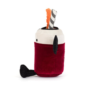 A plush toy shaped like a hot chocolate cup, featuring a deep red velvet body, a cream fabric rim, black ears and nose, and two plush accessories sticking out of the top: an orange textured piece and a gray-and-white striped piece.