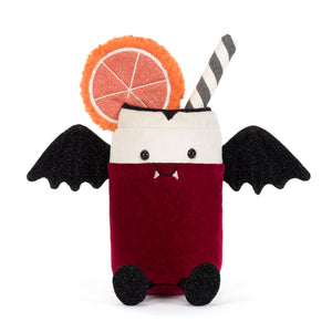 A plush vampire cocktail toy on a white background. The toy features a deep red body, a white head, black bat wings, a black-and-white striped straw, a glittery orange slice garnish, and small black feet.