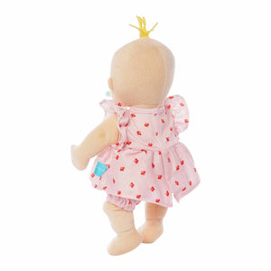 Plush Baby Stella Peach doll with blonde tuft of hair wearing a pink dress and bloomers with cherries print on it. Doll is 15 inches and is standing facing away to give a back view of the velcro fasteners on her dress..