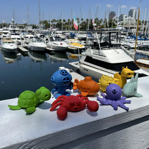 Lifestyle pic of Water Pals bath toys on railing at a marina with boats in the background.