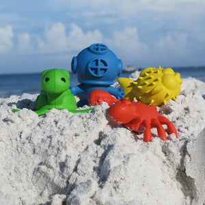 Rubber water pals on sand at seaside. Green sea turtle, blue diver, yellow pufferfish and red crab.