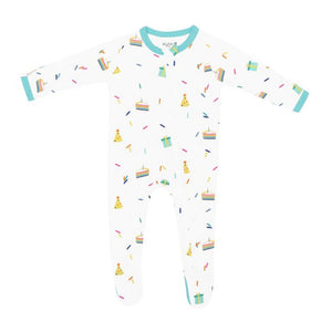 Kyte Baby infant zippered footie with multicoloured cloud party print on a Cloud white background. Zipper down front and one leg with protective zip guard at neck. Robin aqua blue trim at cuffs and neck and on bottoms of non-slip feet over size 6-12m. Cloud Party is a colorful, all-over print featuring rainbow layered cake slices with a lit candle, gift boxes, polka dot party hats, and scattered sprinkles in a rainbow of colors over a white background.