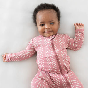 Lifestyle pic of smiling baby wearing dusty rose herringbone printed zip footie.